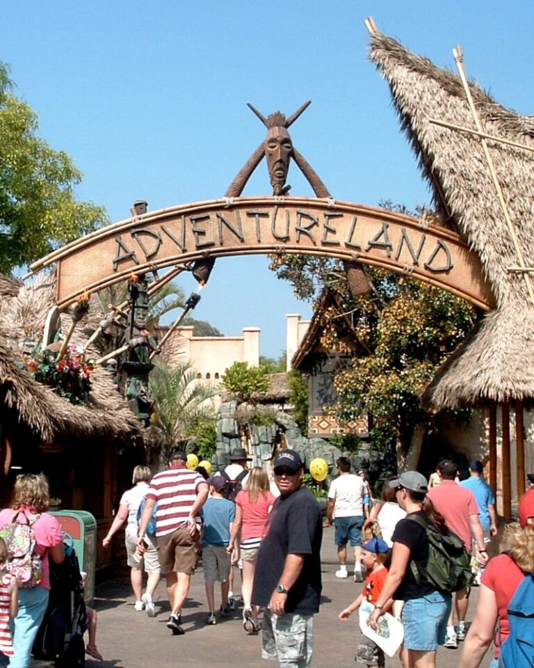 A crowd of people stand beneath a primitive sign outdoors.