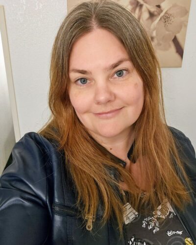 About Me Image Long-haired woman dressed in a blue leather jacket radiates confidence and style, ready to take on the world.